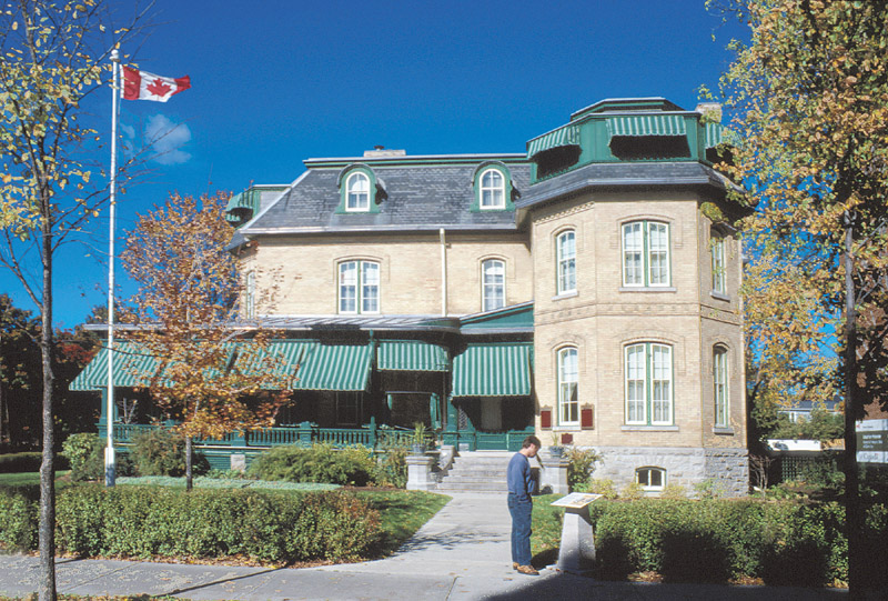 Exterior view of the beige coloured historic home with green awnings and roof, and a croner turret..
